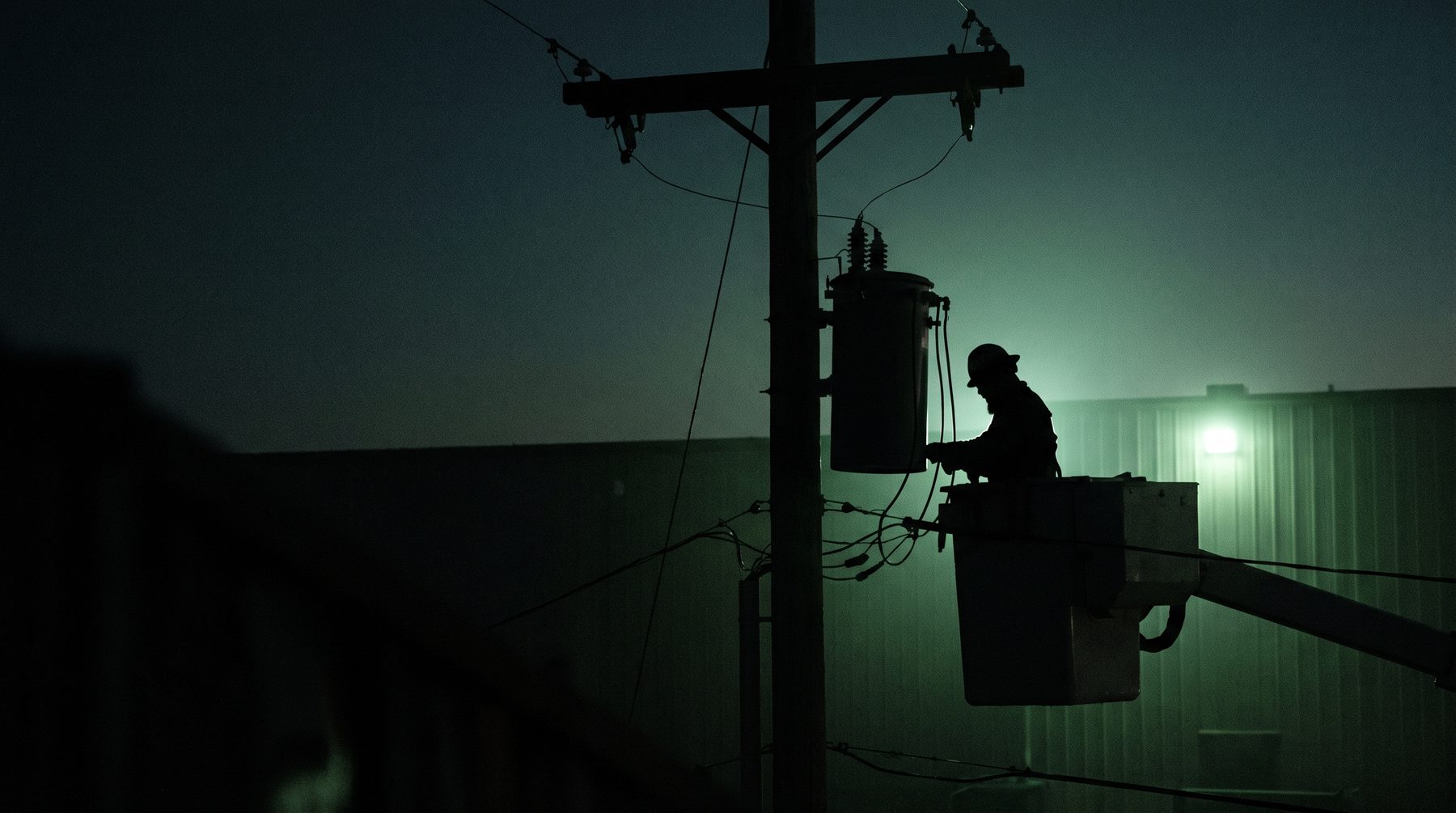 Lineman in a bucket truck at a pole-top transformer, backlit, silhouette